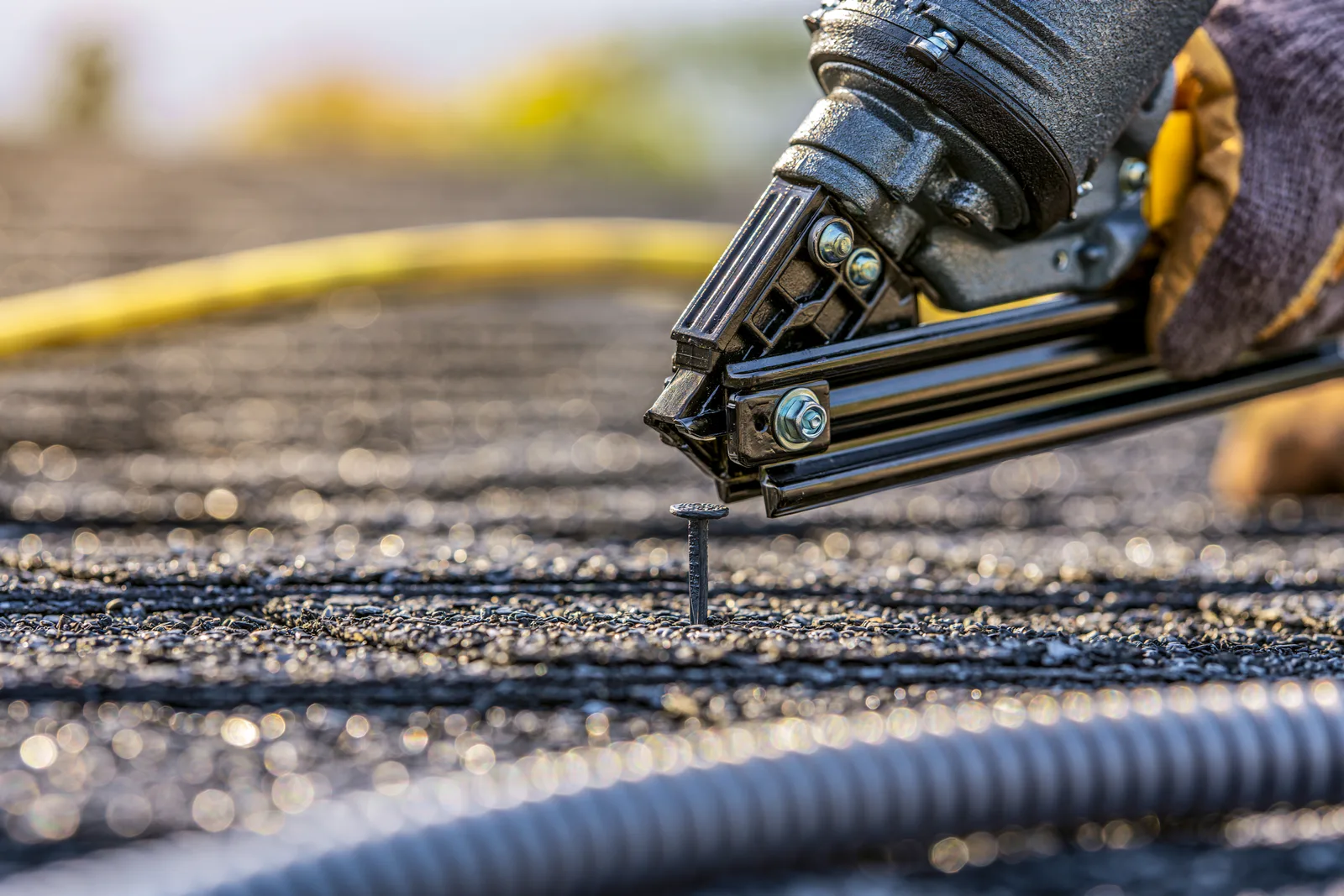 A roofer using a pneumatic nail gun to nail down asphalt shingles