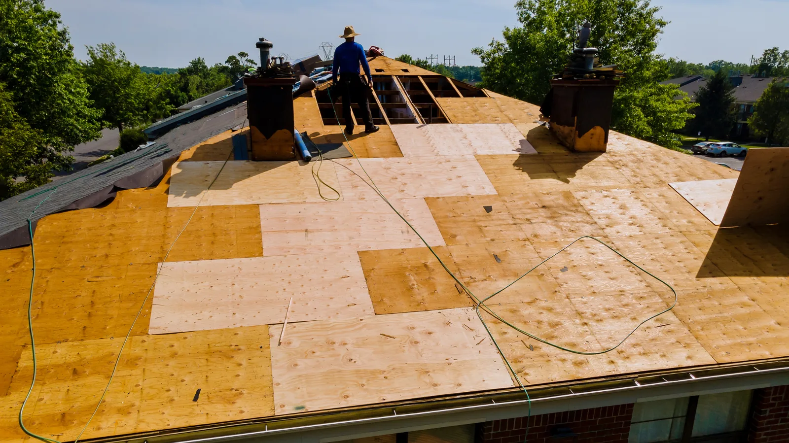 Roofer standing on new plywood decking across a large roof
